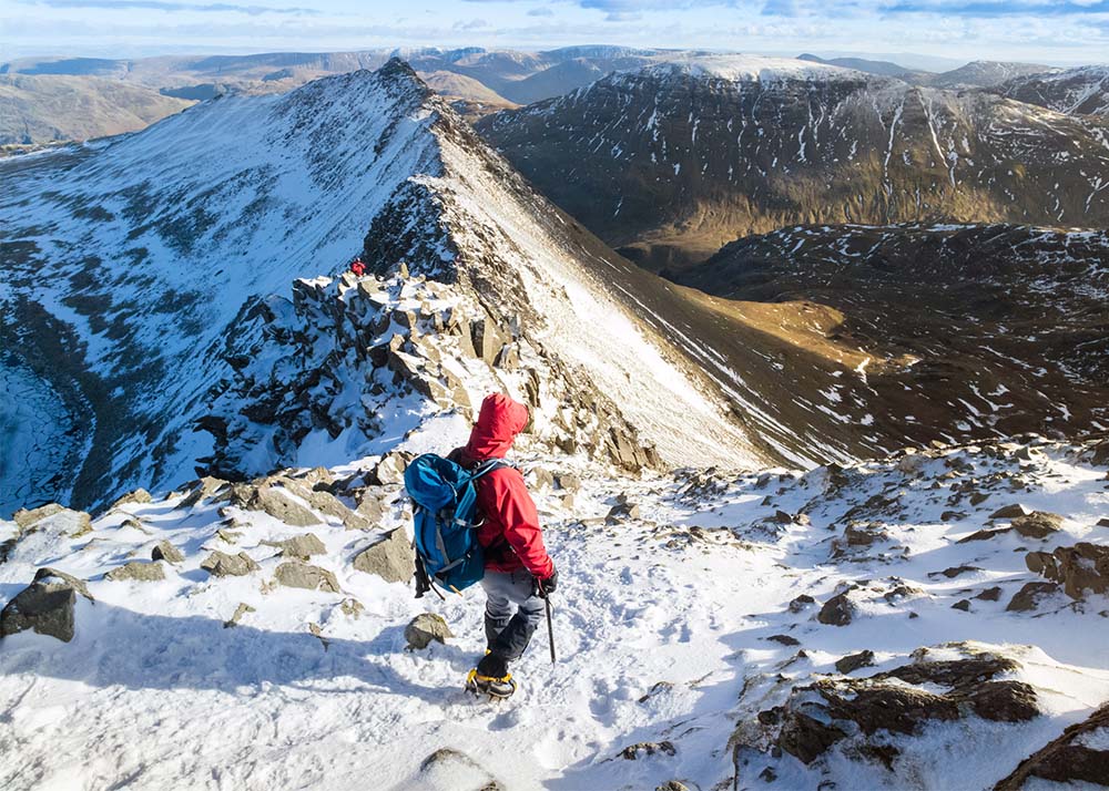 A hiker descending Helvellyn towards Striding Edge and Red Tarn in the Lake District, UK. Winter hiking