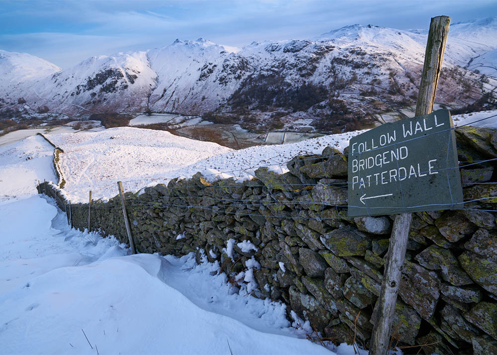 Signpost by a stone wall pointing towards Bridgend, Patterdale in the English Lake District. Winter hiking