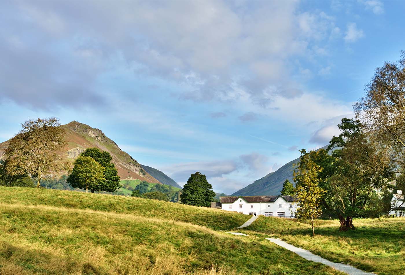 A path winding its way through green fields, from Grasmere, towards Helm Crag, on a tranquil summers day in the English Lake District.